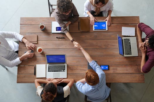 Home Overhead view of colleagues in a work meeting using laptops and tablets, emphasizing teamwork and technology.