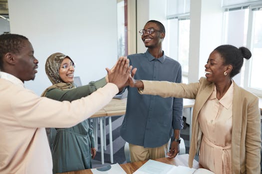 Home A joyful group of diverse colleagues high-fiving each other in an office, symbolizing teamwork and collaboration.